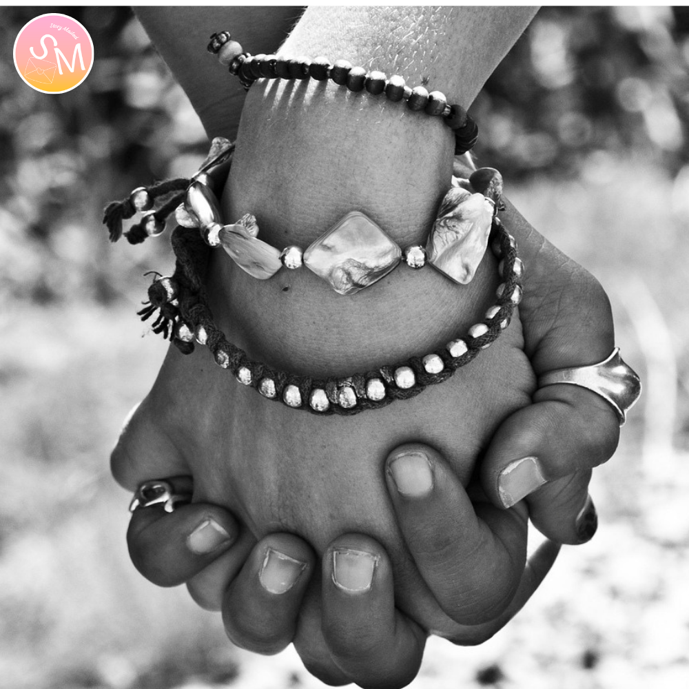 Close-up of hands wearing beaded bracelets with a blurred natural background. lovers holding hands. Maybe We’re All Just Walking Each Other Home story letter series from storymailed